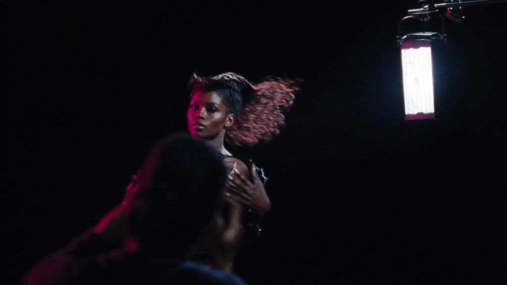 A model mid-movement in a black studio under strobe and magenta rim light