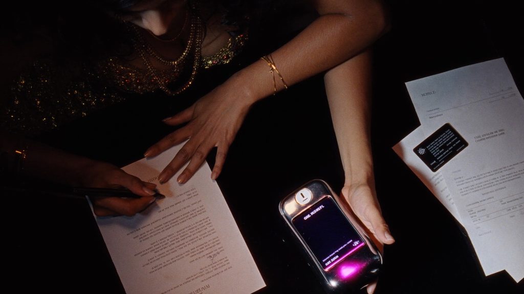 A model signing a one-page contract beside a glowing phone