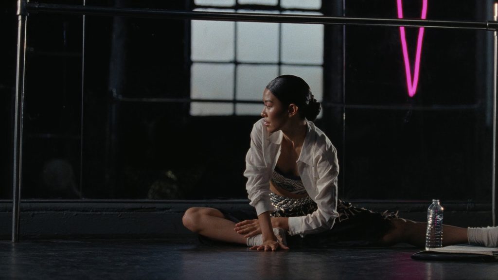 A dancer stretching at a chrome barre in a rehearsal studio at dawn
